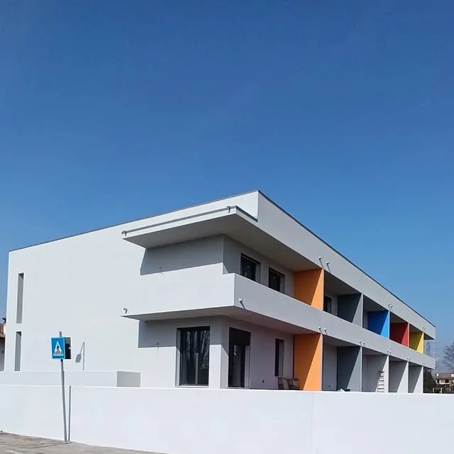 Edificio residenziale completato con facciata chiara e inserti colorati a Porcia